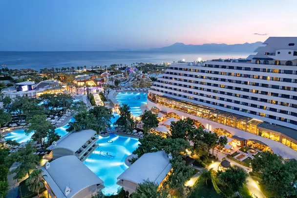 Titanic Deluxe Lara — illuminated pools and ship-style resort at twilight