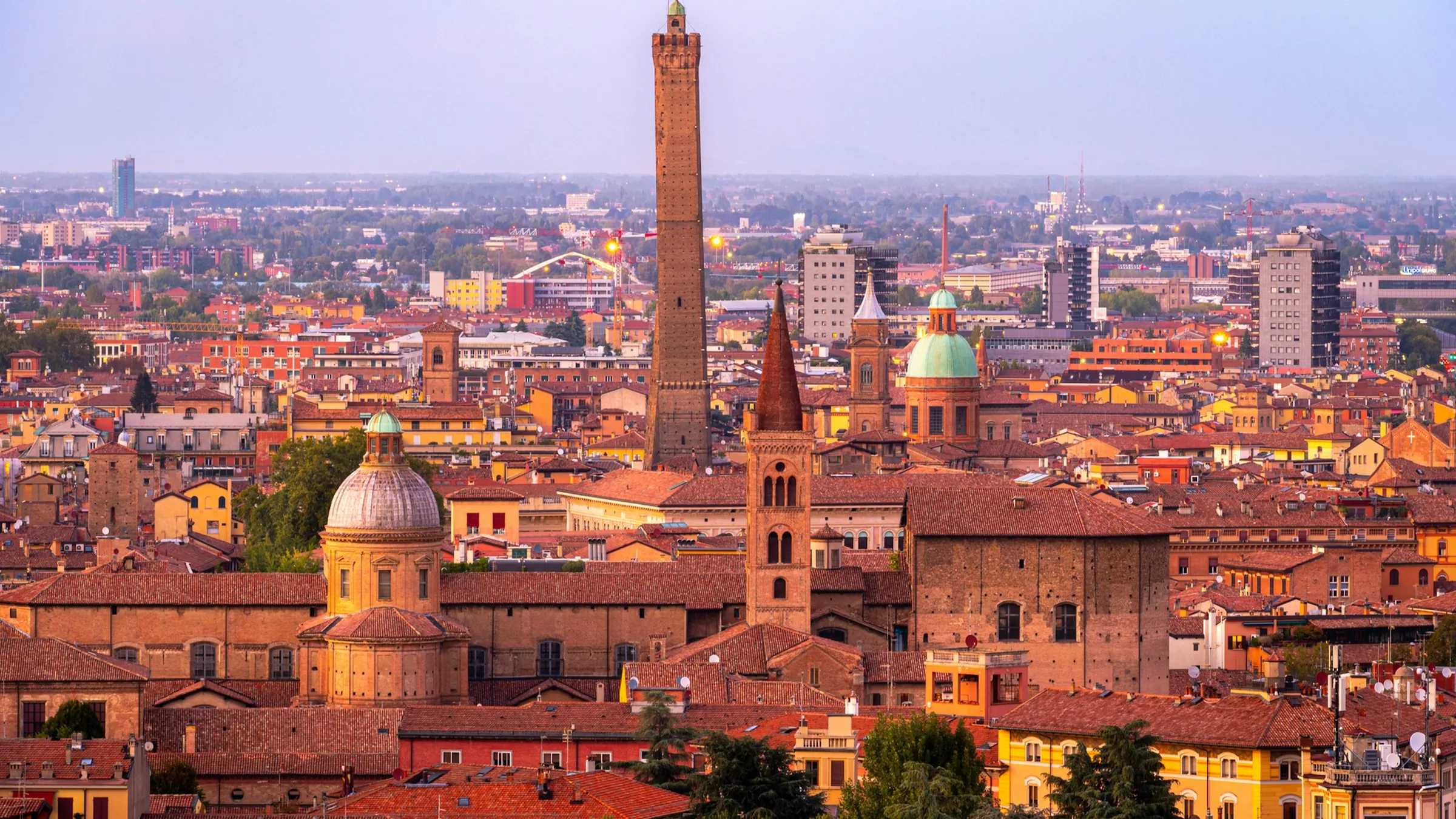 Terracotta rooftops and the Asinelli Tower at sunset across Bologna, Italy
